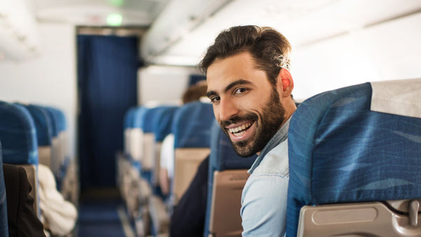 Beard man on a plane, sitting in aisle blue seat looking back and smiling 