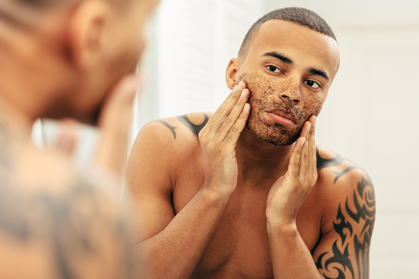 man with tattoo using urth's facial scrub for men