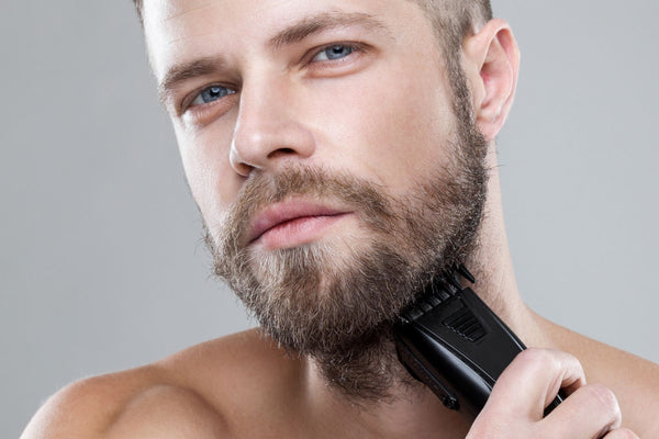 Man with short beard holding electric shaver in bathroom