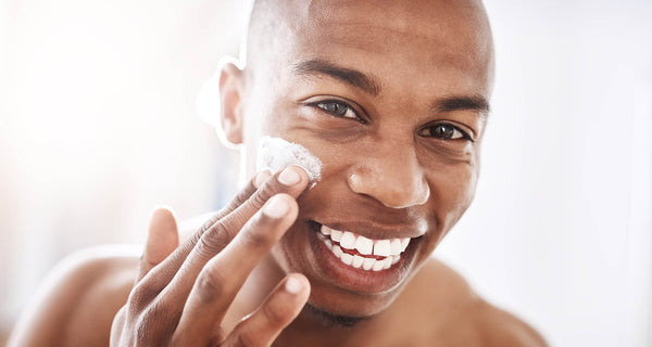 HANDSOME BLACK MAN SMILING AND APPLYING MOISTURIZER TO FACE